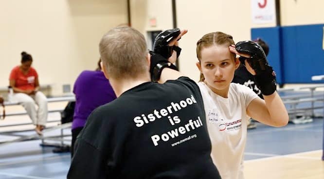 two people sparring, the t-shirt that one person is wearing reads, Sisterhood is Powerful